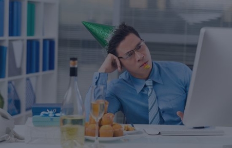 A man with a party hat and champagne sitting at his desk upset.